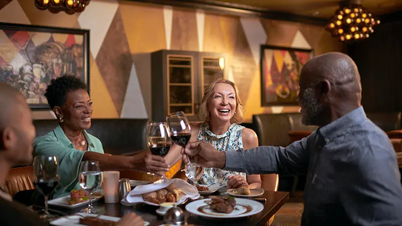 Guests dining at Chops Grill and toasting with a glass of red wine.